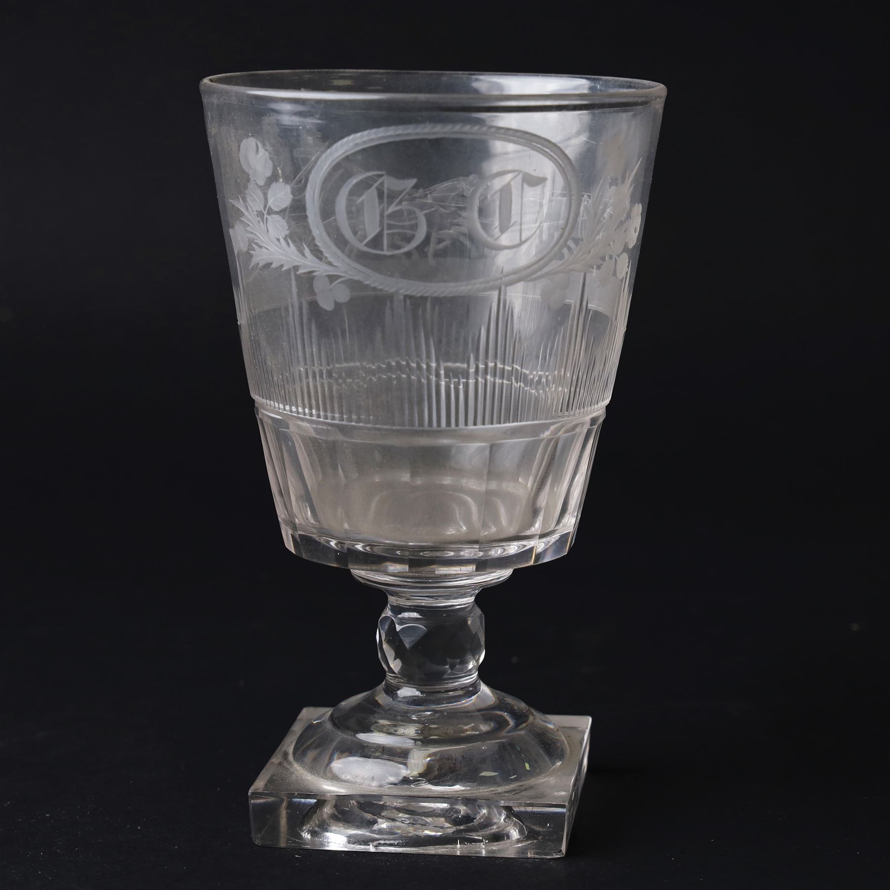 Early 19th century glass rummer, the deep bucket shaped bowl engraved with an oval roundel containing initials BC flanked by flowers of the Union, and a carriage drawn by four horses, above cut fluted and vertical cut bands, upon a short diamond cut knop stem, and square base, H15cm