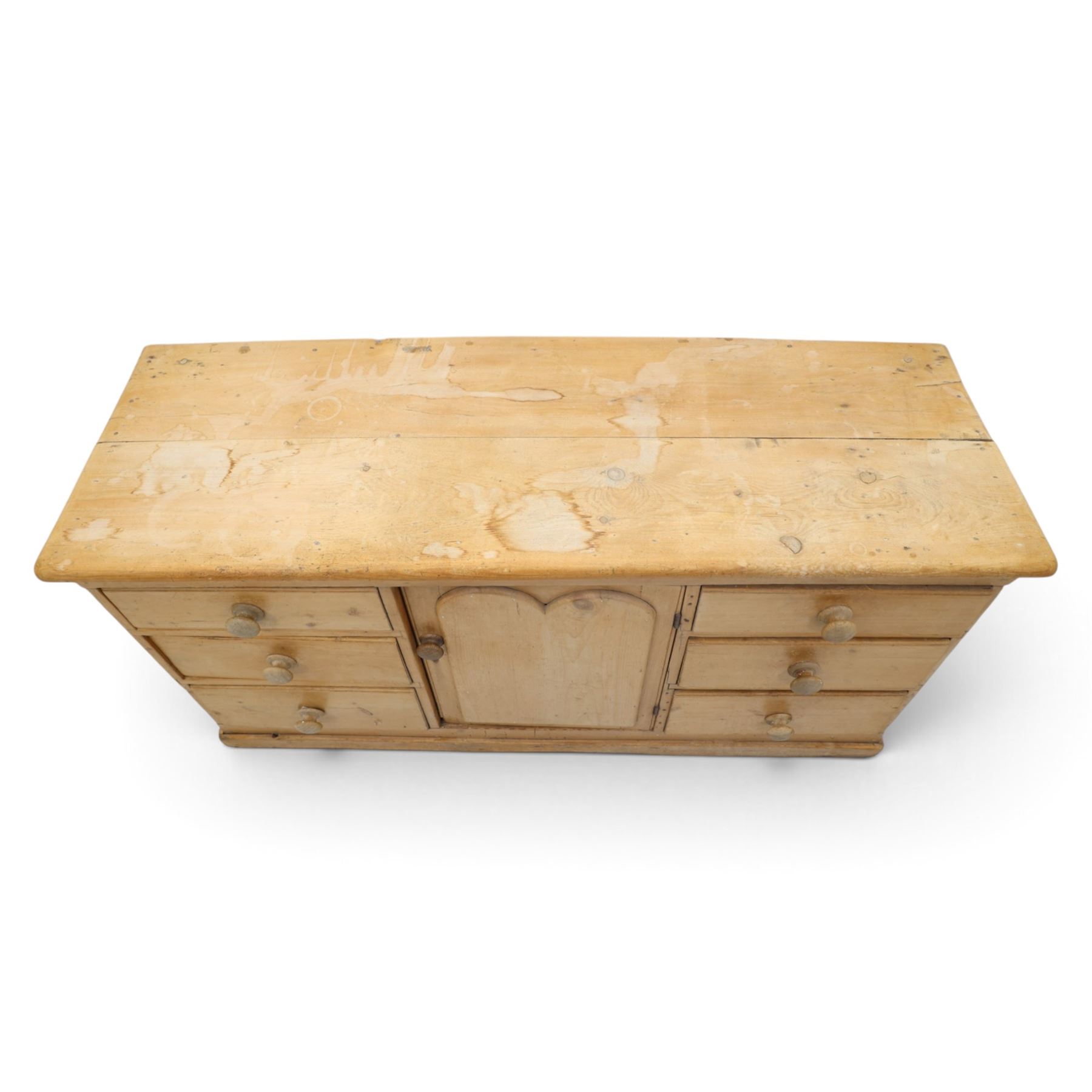 Victorian stripped pine sideboard, rectangular plank top rounded edges, with central cupboard door with shaped panel, flanked by two banks of three graduating drawers with turned knobs, raised on a plinth base 