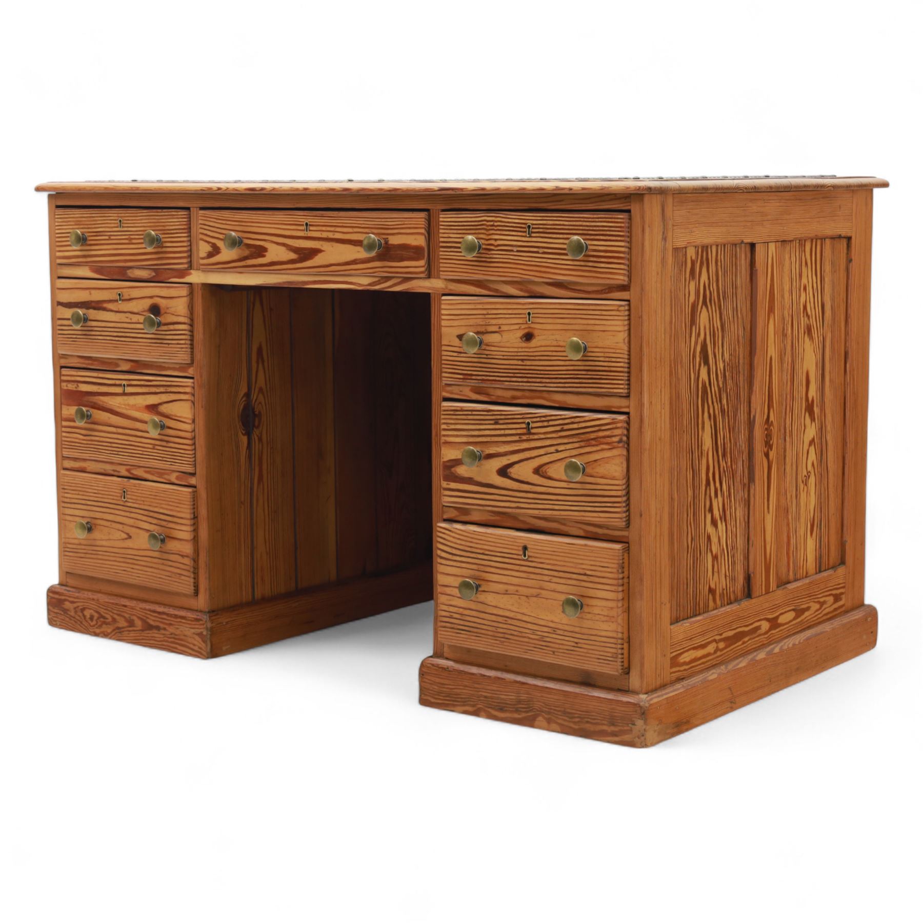 Contemporary stripped and waxed pine pedestal kneehole desk, rectangular top inset with green leather writing surface with brass studded edge, fitted with nine drawers with brass knob handles, above a plinth base on recessed castors