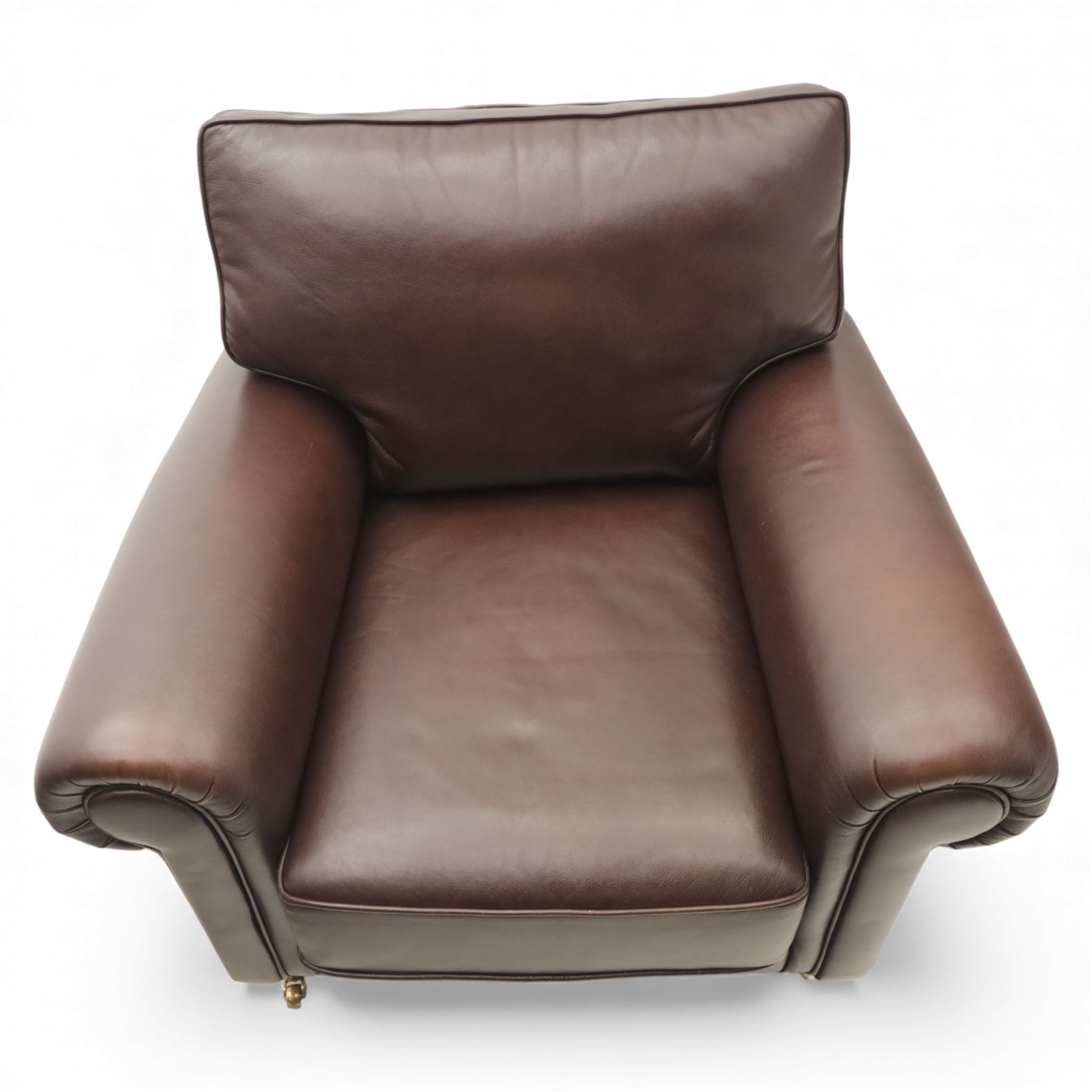 Laura Ashley - brown leather armchair and foot stool, loose cushion back and seat, flanked by scrolled arms upon light stained wood supports on castors, matching brown leather footstool with four panel top over light stained supports on castors (Footstool H 31cm, W 52cm)