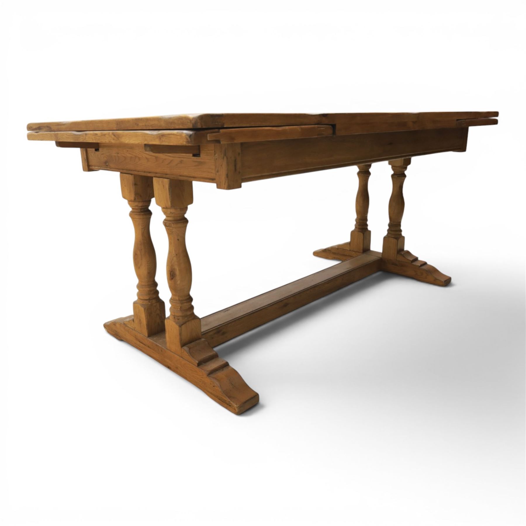 Traditional oak refectory dining table, fitted with draw leaves to either end extending to 257cm, on twin turned and block supports united by a stretcher, terminating in shaped trestle feet