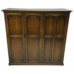Early 20th century oak triple wardrobe, three panelled doors with geometric mouldings and fretwork spandrels, the interior fitted with slides and hanging rail