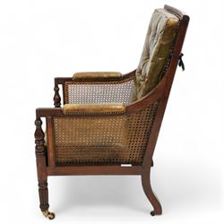 George IV mahogany framed library reading chair, reed moulded frame with cane work seat, back and sides, with loose cushions upholstered in green buttoned leather, upholstered arm rests, turned arm supports terminating to turned and reed carved feet, on castors 