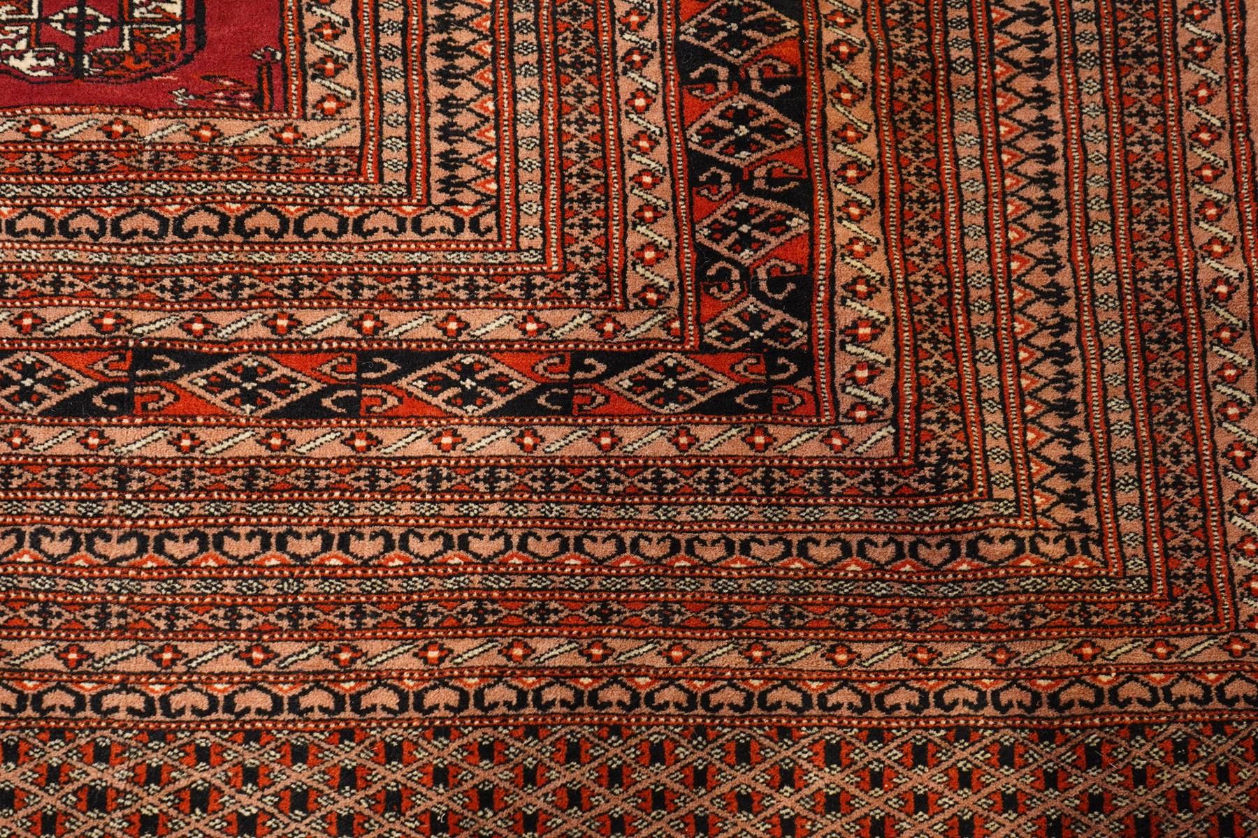 Large Afghan Bokhara crimson ground carpet, the field with rows of repeating Gul motifs and geometric design, enclosed by multiple repeating geometric guard bands