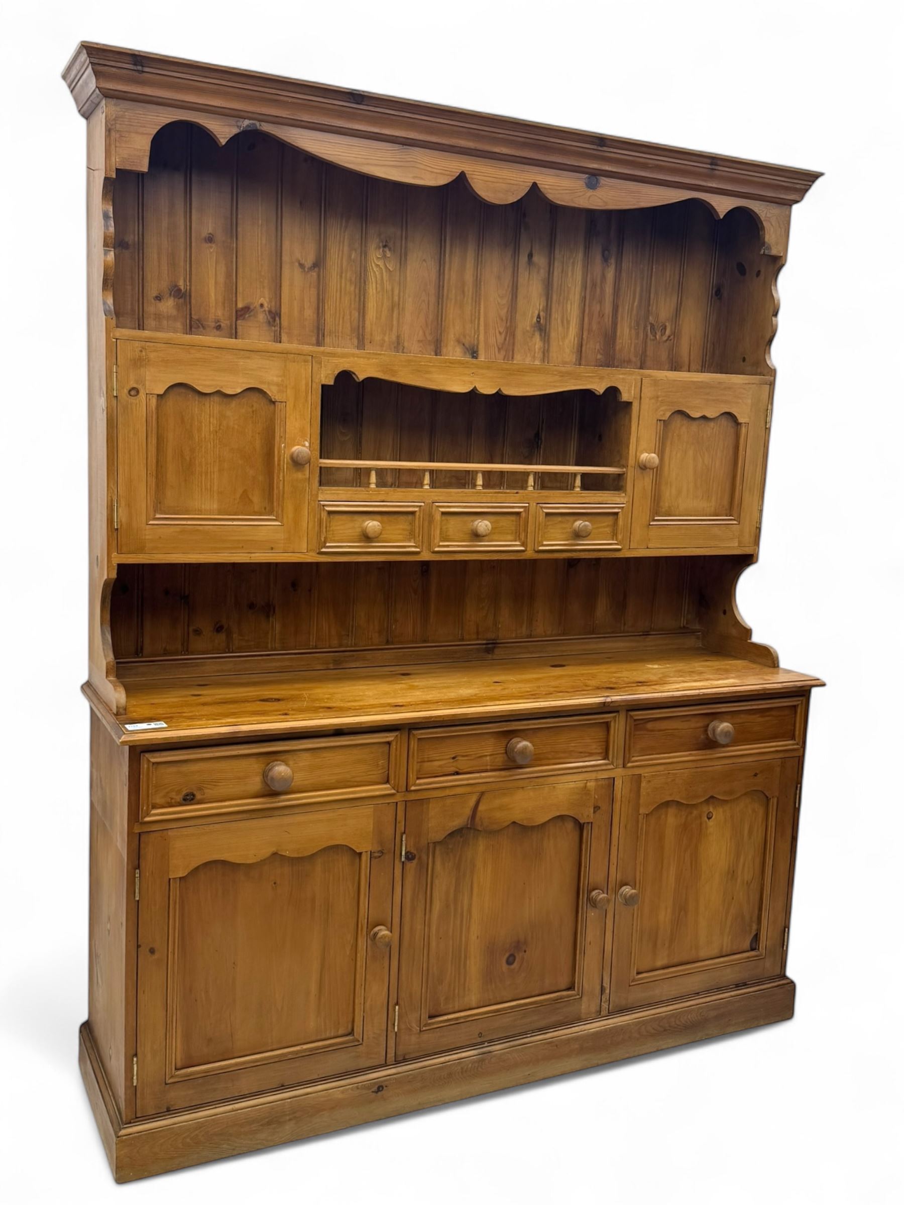 Traditional vintage pine kitchen dresser with scrolled cornice and rack with long shelf above a galleried shelf flanked by three short drawers and two cupboards, the base with three long drawers above three cupboards on plinth base  