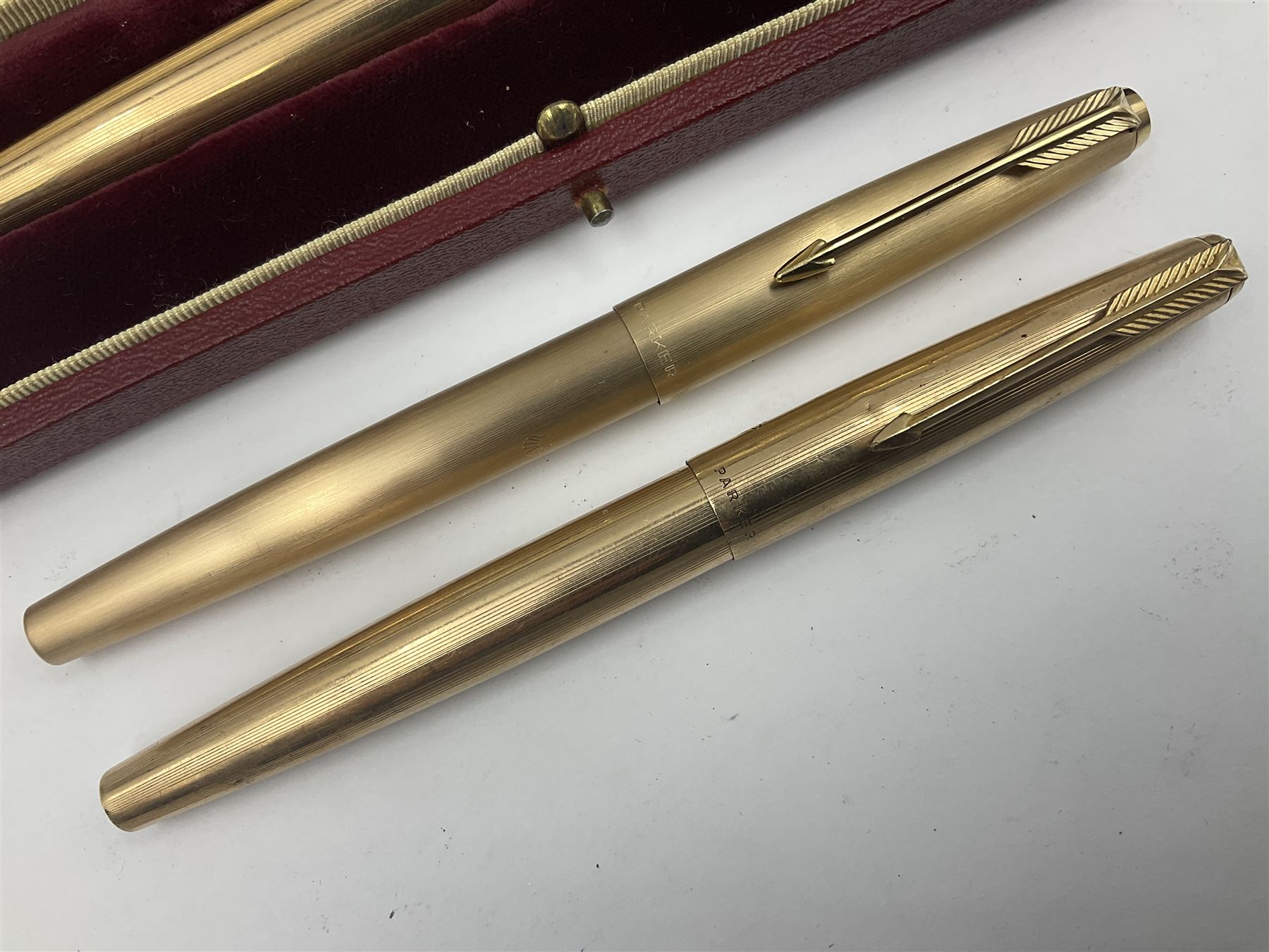 Three rolled gold Parker fountain pens, comprising an example with a gold nib marked 14K 585 and barrel with a shell stamp, a Parker 61 fountain pen with inset gold arrow to the nib, and another similar, all with striated decoration and arrow clips to the caps, L13cm, one with box