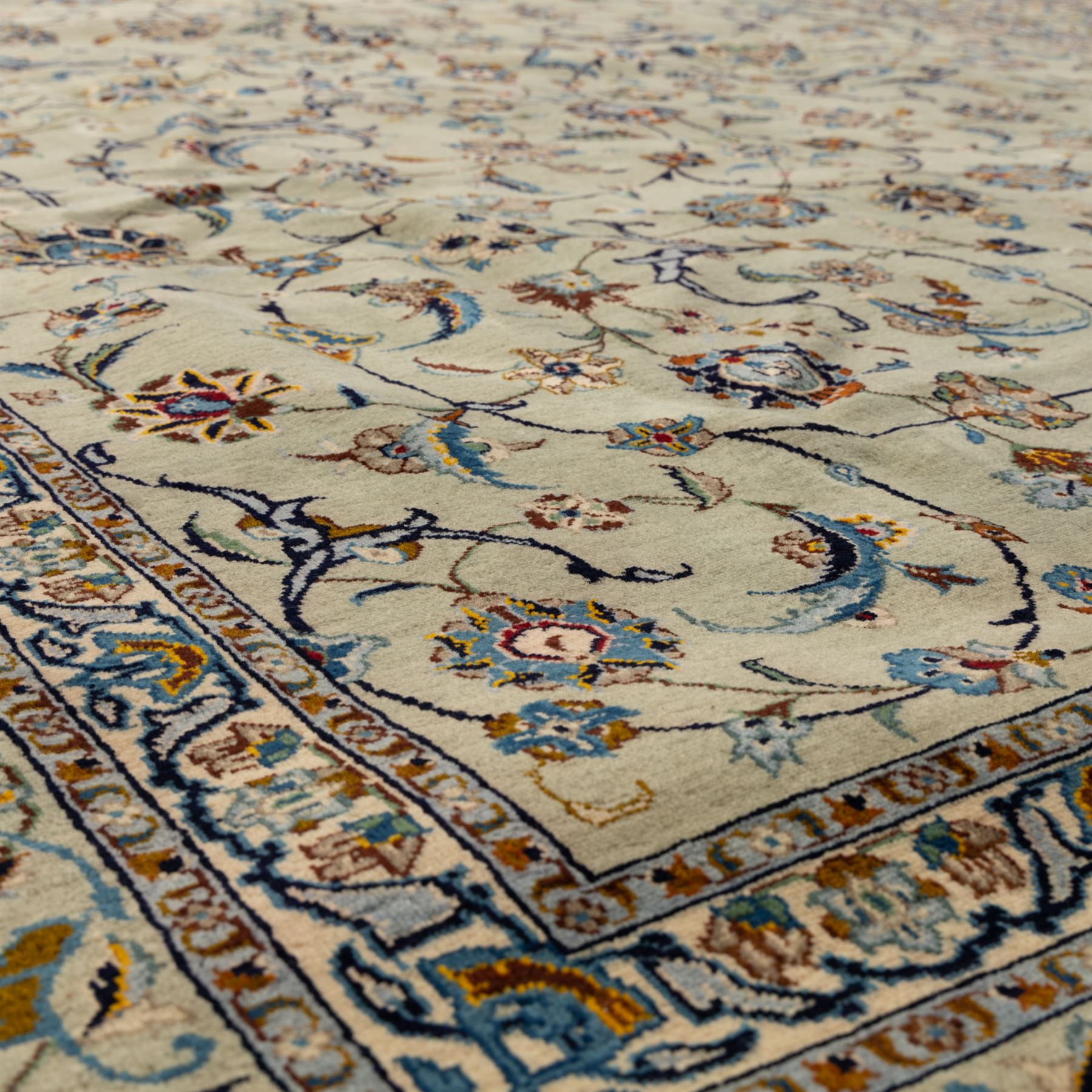 Persian Kashan rug, cream ground decorated with an all-over pattern of interlaced floral stems, rosettes and palmettes in blue, gold and rust tones, framed by layered floral borders, woven in the Kashan region of Iran