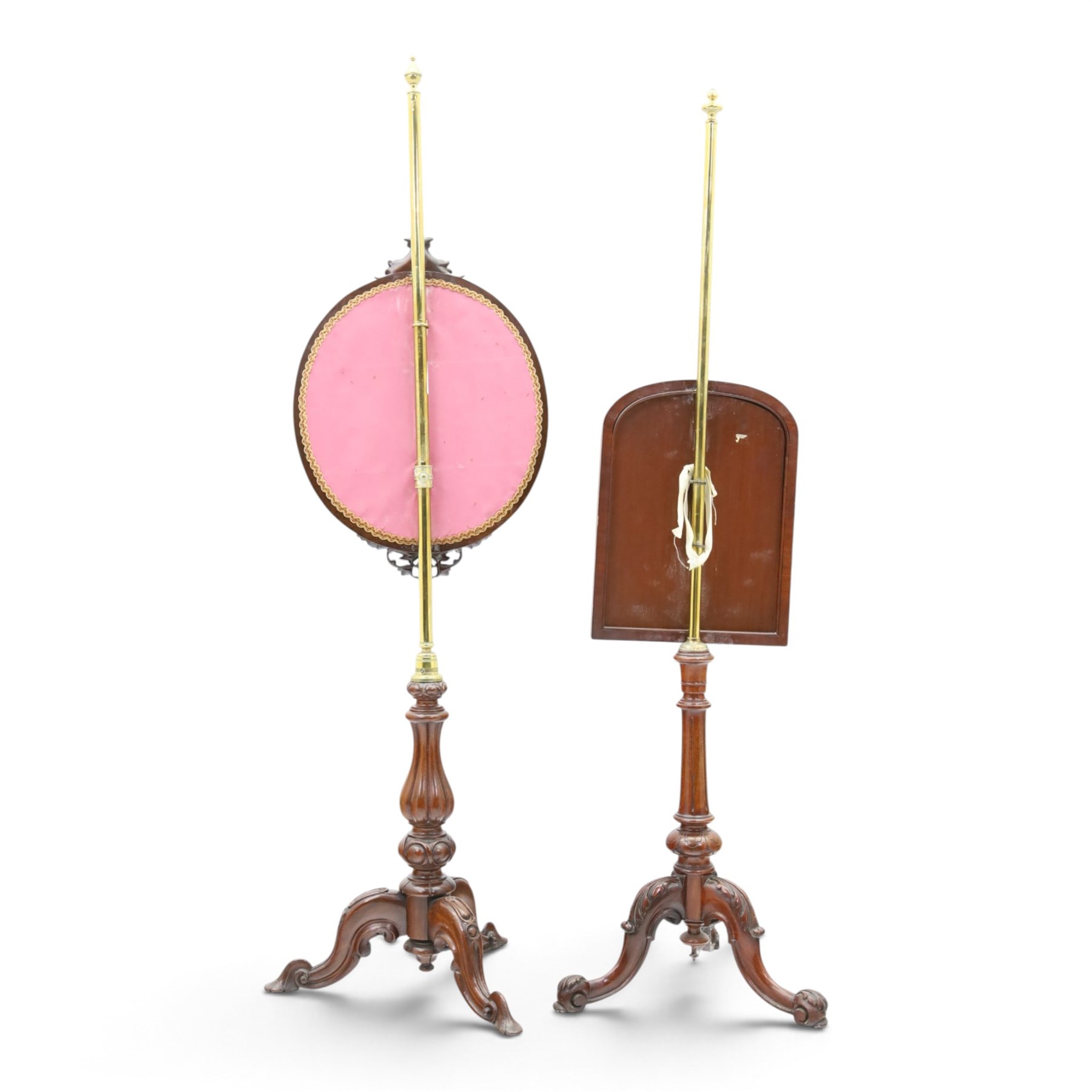 Two Victorian mahogany pole screens, comprising an oval example with floral needlework panel and carved cresting, on brass pole and tripod base with scroll carved supports (H 153cm, W 43cm, D 43cm); and a rectangular example with glazed architectural print panel, on brass pole, turned column and conforming scroll carved tripod base (H 147cm, W 38cm, D 38cm)