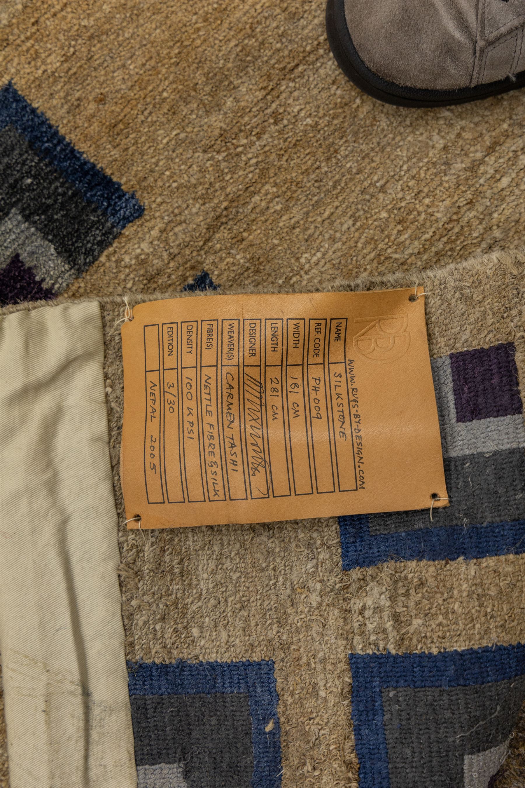 Rugs by Design - ‘Silk Stone’ Nepalese thick pile wool rug, with plain textured camel ground and geometric border detail in blue, grey and dark tones to two sides