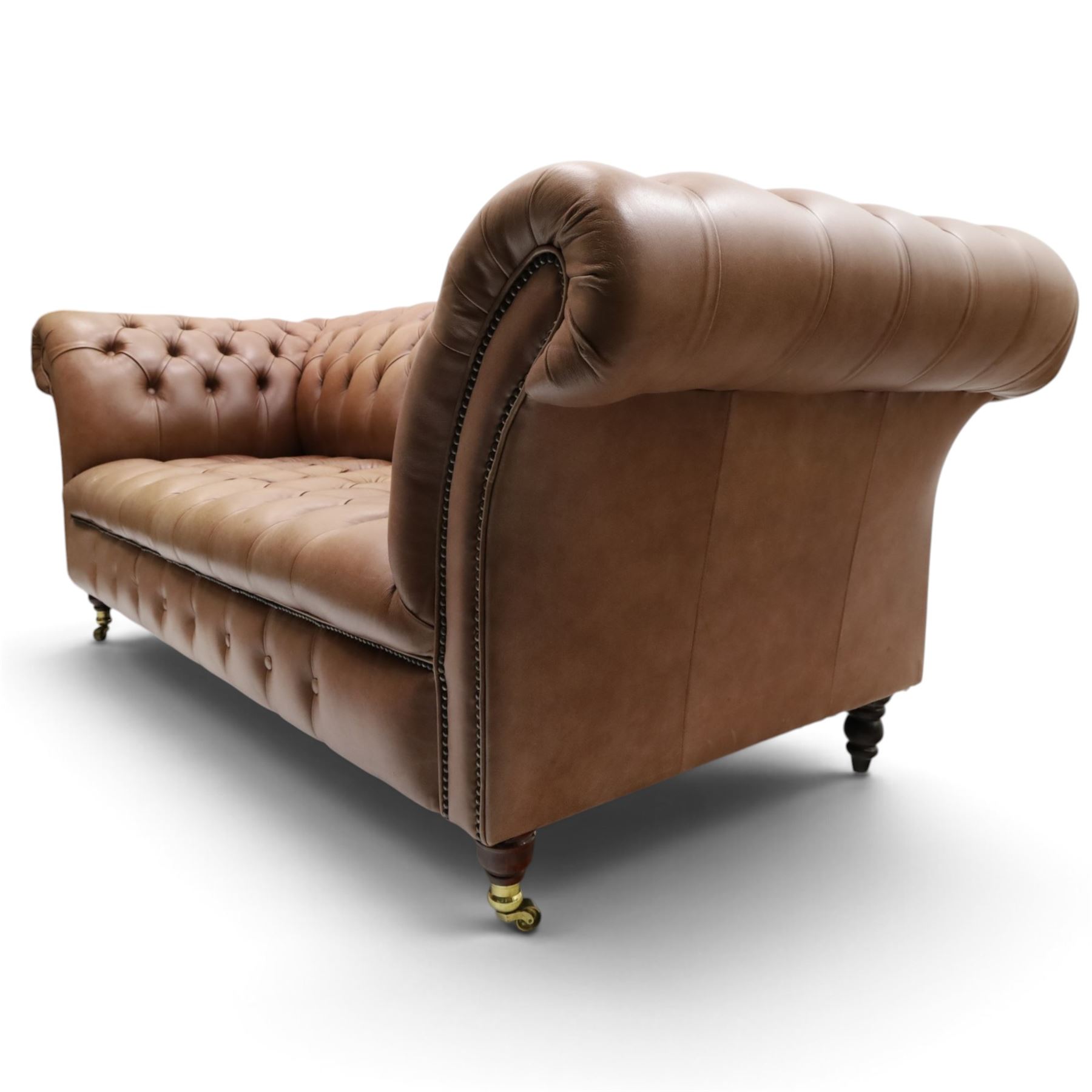 Distinctive Chesterfield - full buttoned tan brown leather sofa, deep buttoned back, seat and arms, raised on dark stained supports terminating in brass castors 