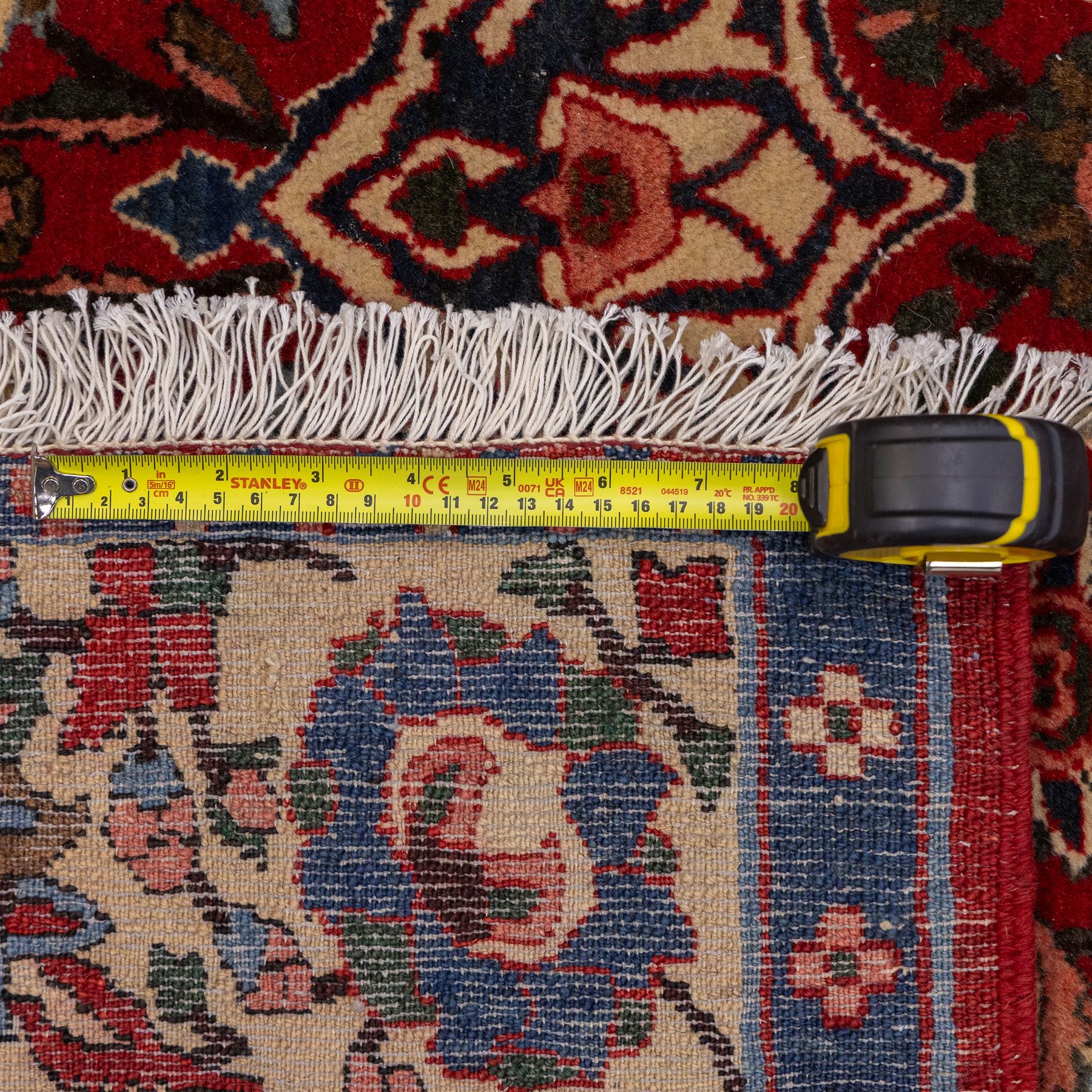 Central Persian Isfahan hand-knotted rug, madder red field, with elaborate central medallion with pendants and scrolling arabesques, palmettes and stylized floral sprays arranged in a densely ornamented ground of classical Safavid inspiration, ivory border with a continuous vine scroll of palmettes and rosettes, flanked by multiple guard stripes in navy and red with geometric and floral motifs, with cotton fringe ends 