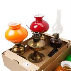 Table oil lamp with red glass reservoir on metal base, three other oil lamps and various shades and chimneys