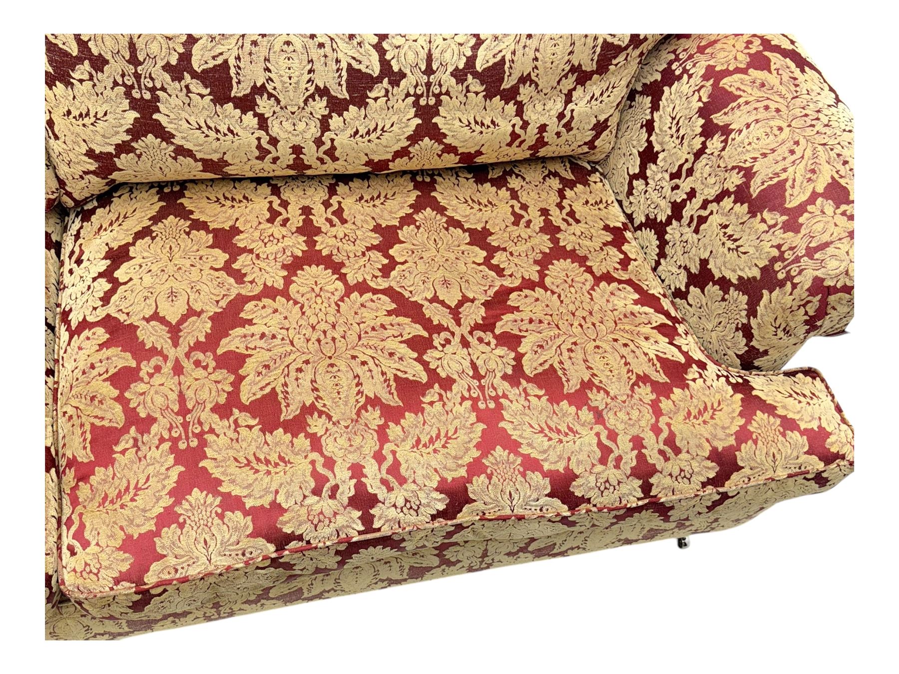 Duresta - pair of Grande three-seat sofas, traditional shaped with rolled arms and upholstered loose cushions, in red ground fabric with raised gold foliate pattern, on turned feet with brass castors 
