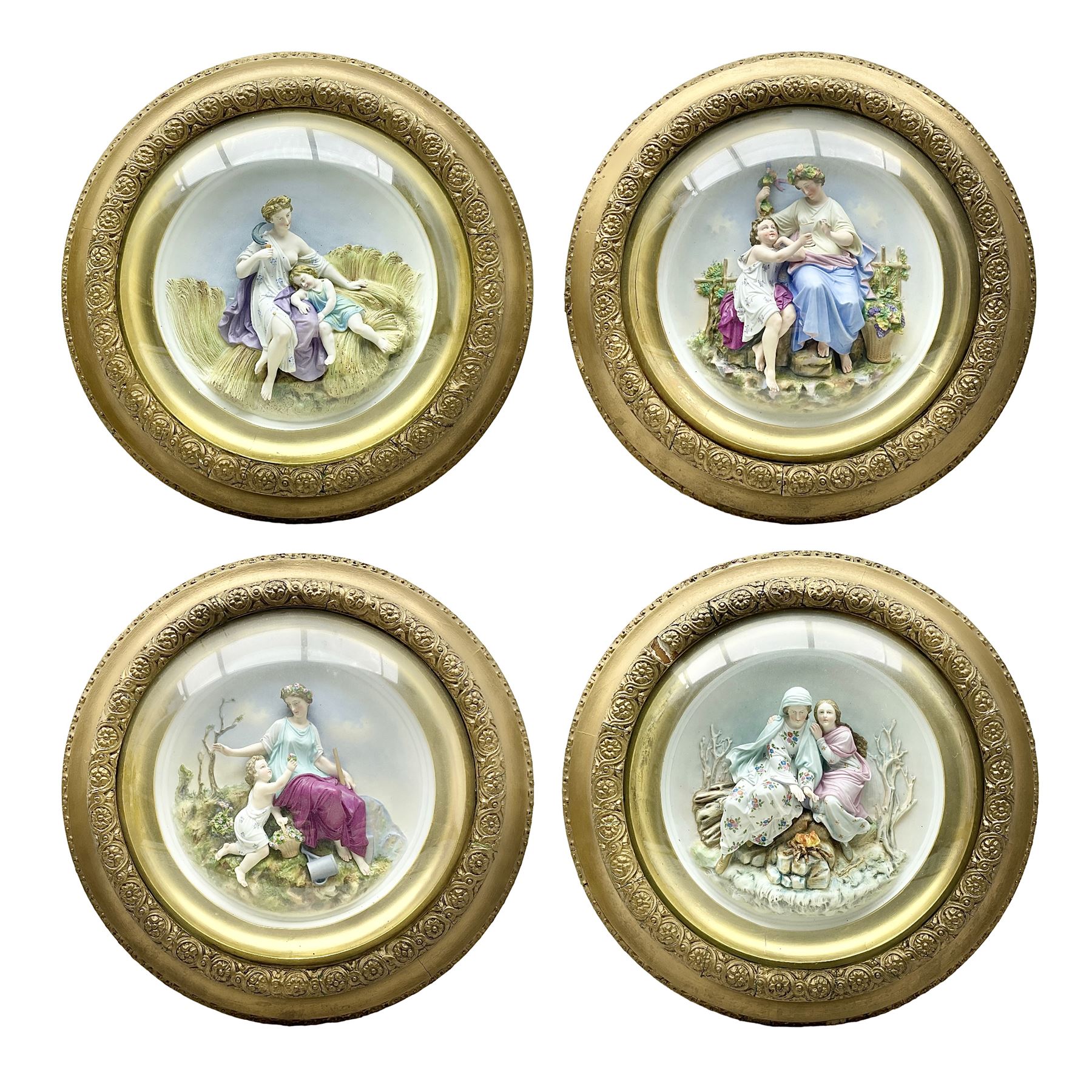 Set of four early 20th century Continental bisque plaques, each of circular form, modelled in high relief as the Four Seasons personified, within gilded circular frames under convex glass, overall D44.5cm