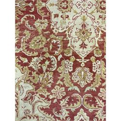 Persian design beige and crimson ground rug, the field decorated with interlacing scrolled foliage, repeating border within guard stripes 