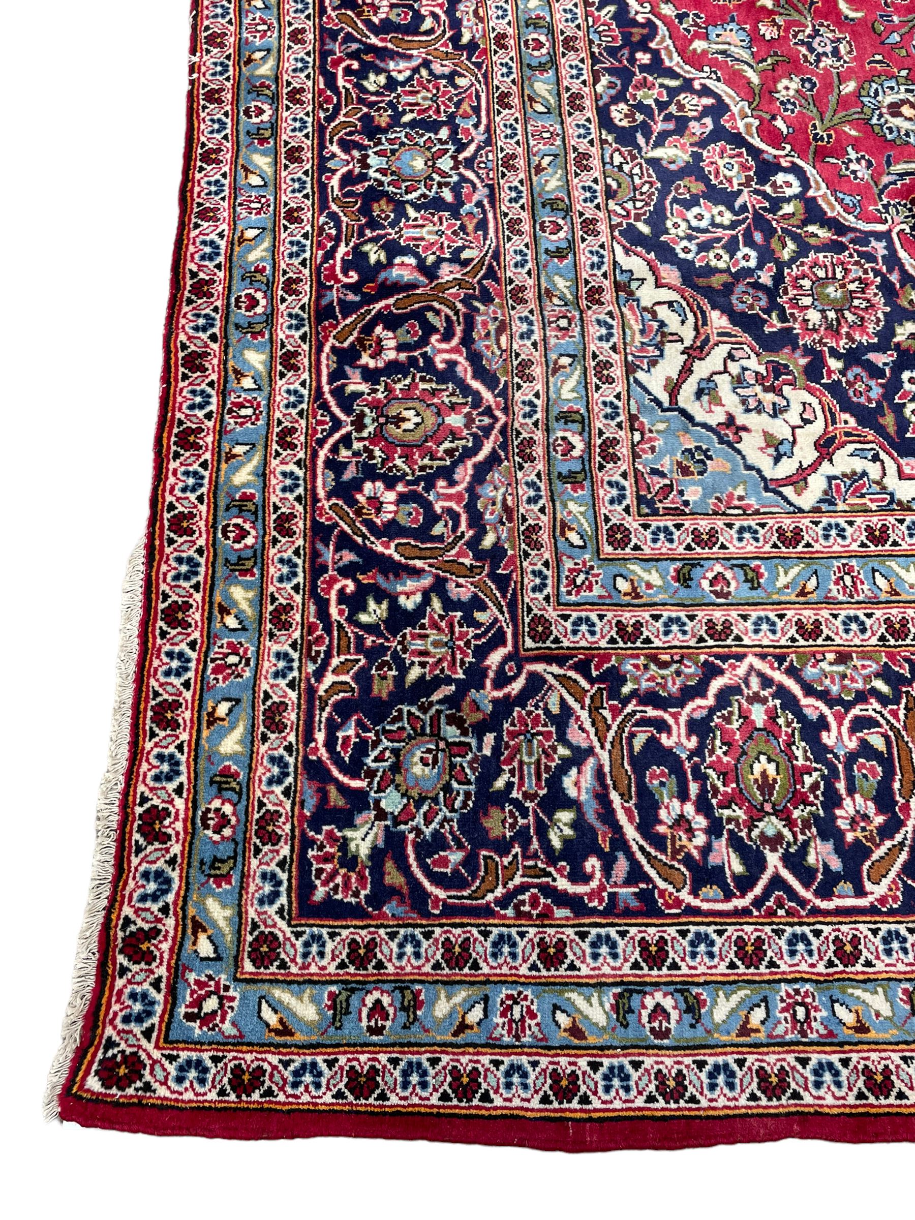 Central Persian Kashan crimson ground carpet, central  floral pole medallion with matching spandrels within a field of scrolling palmette motifs and foliage, the heavily banded indigo border with repeating plant motifs interlaced with scrolled branches