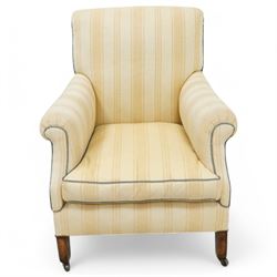 Early 20th century scroll arm armchair, upholstered in ivory striped cotton fabric with piped seams, sprung seat, on turned tapering front legs with brass caps and castors