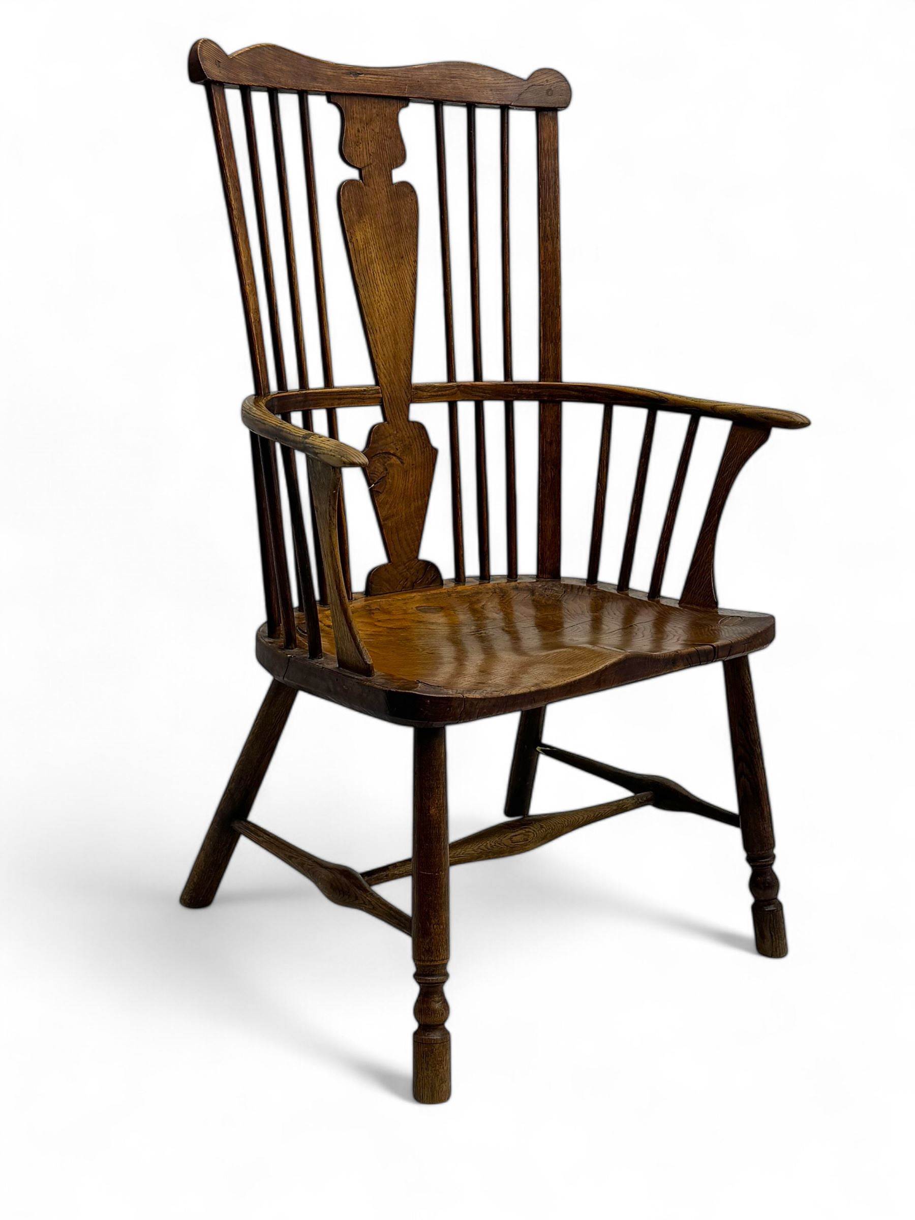 Early-to-mid 19th century elm and ash high-back Windsor armchair, central vase-shaped splat flanked by slender vertical spindles, outward-curving arms, shaped and dished saddle seat, raised on turned and splayed supports united by H-stretcher
