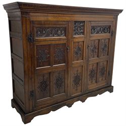 Large 18th century and later oak livery cupboard, projecting moulded and dentil cornice, sunken fillet moulded frame, triple vertical panelled central upright, enclosed by two doors each with five panels, the top row of panels carved with stylised scrolls, the lower panels carved with foliate lozenges, on shaped bracketed skirt base 