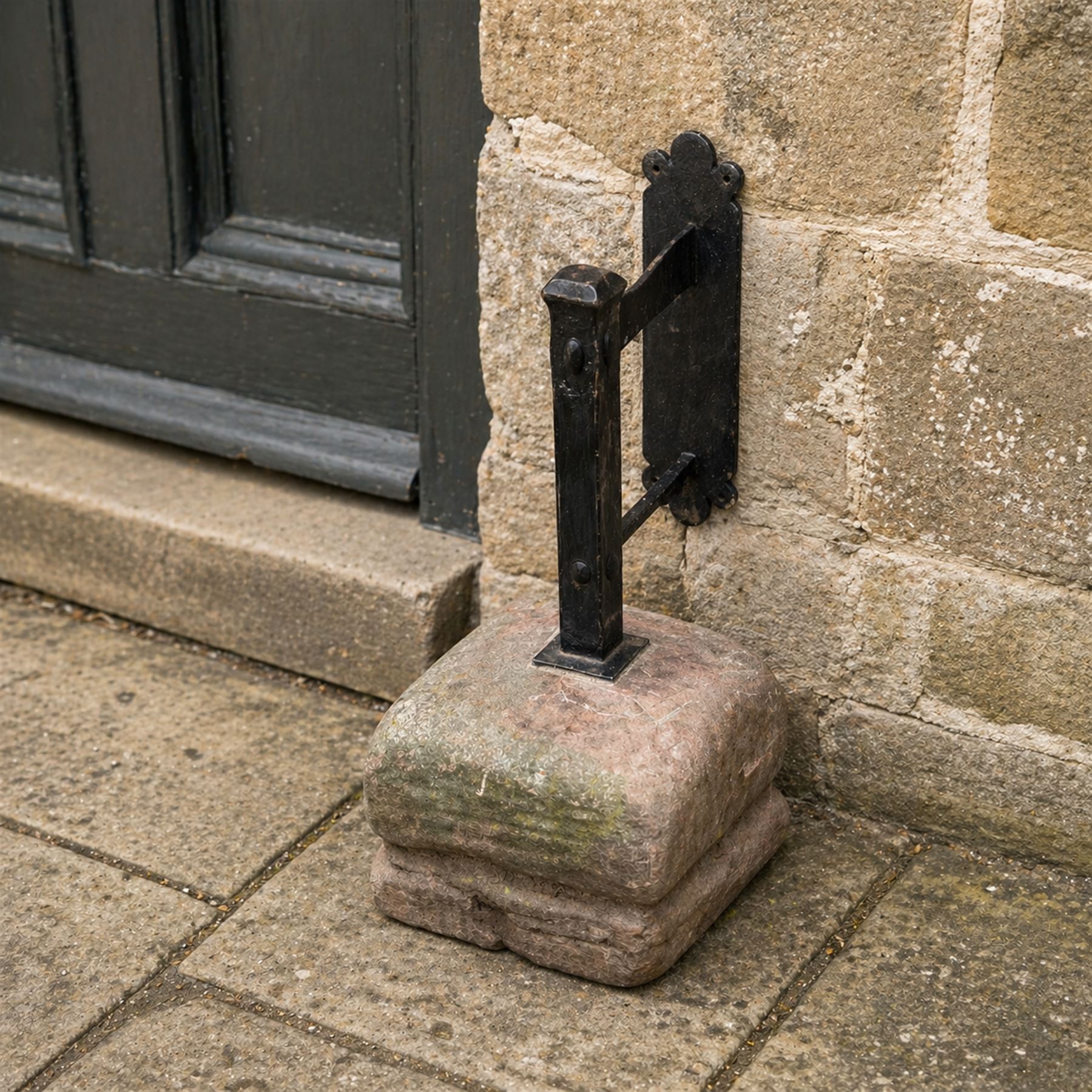 Large wrought metal boot scraper in black painted finish, set in formed stone plinth
