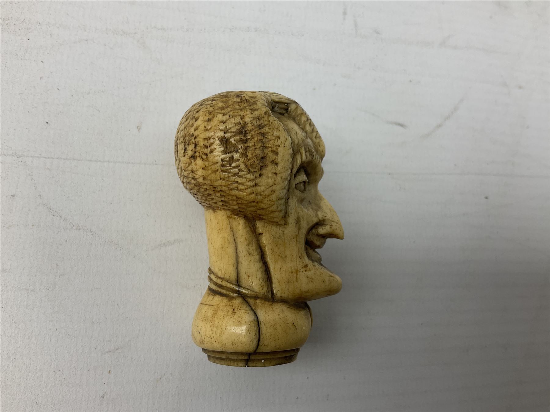 19th century carved ivory walking cane handle, modelled as the head of a greyhound with inset glass eyes, together with a further 19th century ivory example, modelled as a caricature of a gentleman's head, (2)