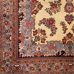 Central Persian Kashan hand-knotted carpet, cream ground, with a central lobbed floral burgundy, rose, and indigo medallion, surrounded by scrolling sprays of carnations and palmettes, with sky blue spandrels decorated with curvilinear vines and stylized blossoms, framed by a repeating terracotta border of palmettes, framed by narrow guard stripes 