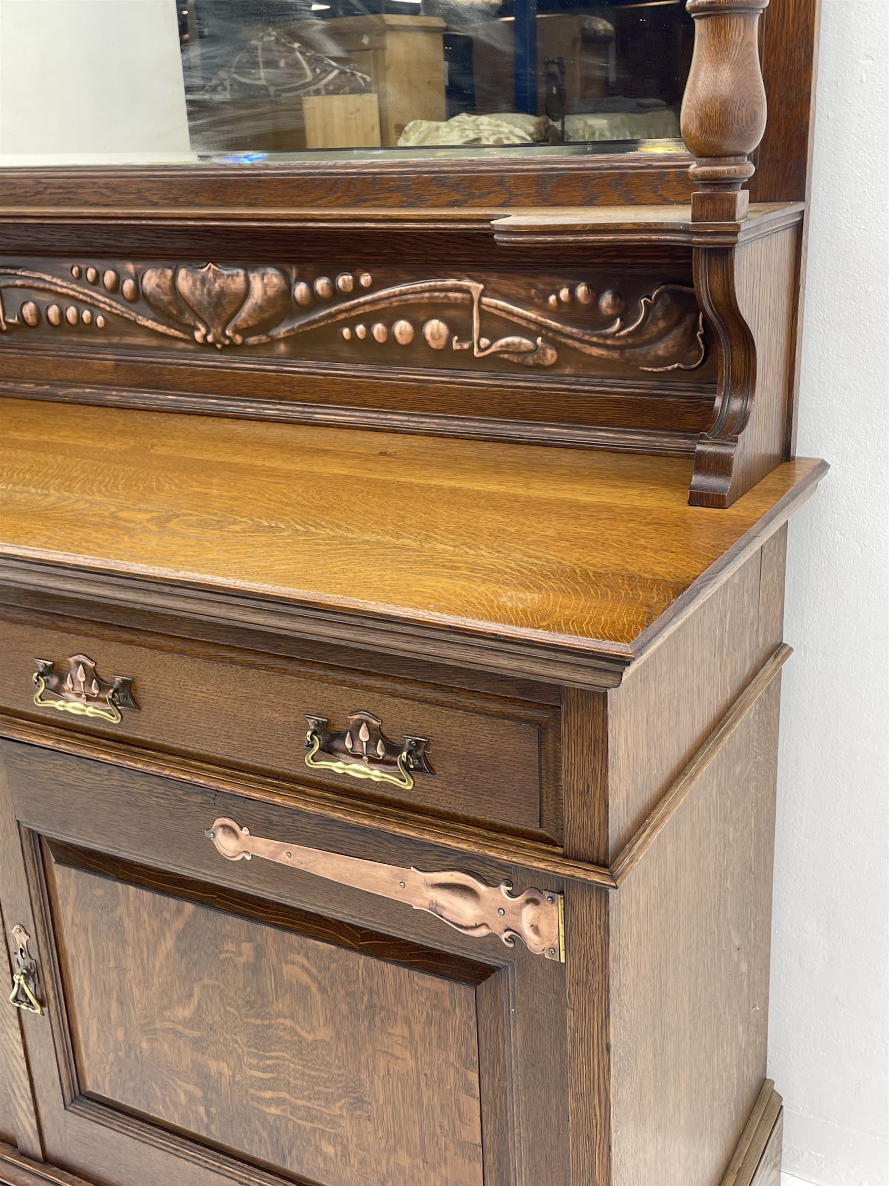Arts and Crafts period oak mirror back dresser, projecting cornice above rectangular bevelled mirror and shelf, two turned supports, inset copper panel with embossed decoration, rectangular moulded top over two drawers and two panelled cupboard, moulded plinth base, brass and copper strappings and handles 