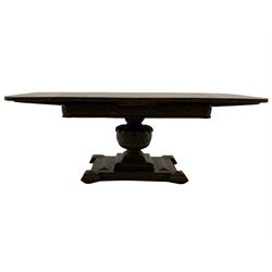 Early to mid 20th century oak drawer leaf extending dining table, the top with quarter book matched veneers over frieze carved with trailing vine, gadroon carved baluster pedestal on geometric platform, turned compressed bun feet
