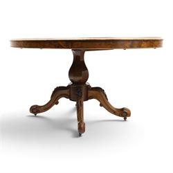 Victorian figured and burr walnut loo table, oval book-matched veneer top with moulded edge, over a turned octagonal pedestal terminating to four splayed supports with flowerhead carved knees and scroll feet with castors