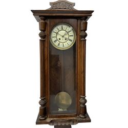 German spring driven wall clock c 1910, with an eight day Gustav Becker movement striking the hours on a coiled gong, in a walnut case with a flat top and carved pediment, fully glazed door flanked by turned columns, two part enamel dial with roman numerals, gothic hands and spun brass bezel, with pendulum and beat plate.