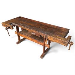 Large early 20th century rustic stained reclaimed pine workbench, the substantial plank top with recessed tool well and two homemade wooden screw vices, above a single frieze drawer and slatted undertier, raised on trestle end supports