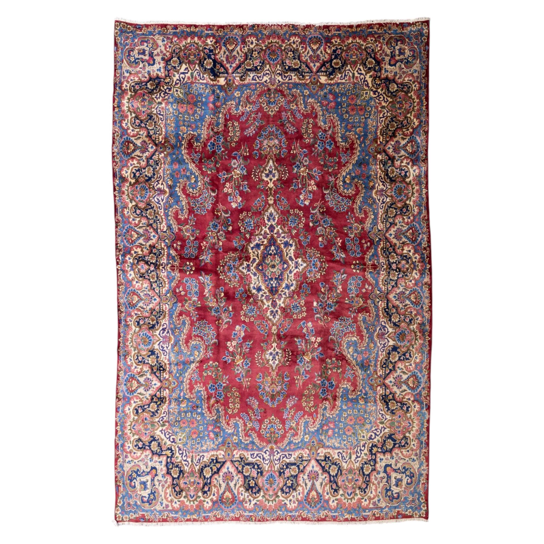 Large Central Persian Kirman hand-knotted carpet, raspberry red field, with central shaped medallion surrounded by an intricate arrangement of scrolling vines and floral sprays, within conforming spandrels and a pale blue border decorated with floral motifs, enclosed by guard stripes, with cotton fringe ends 