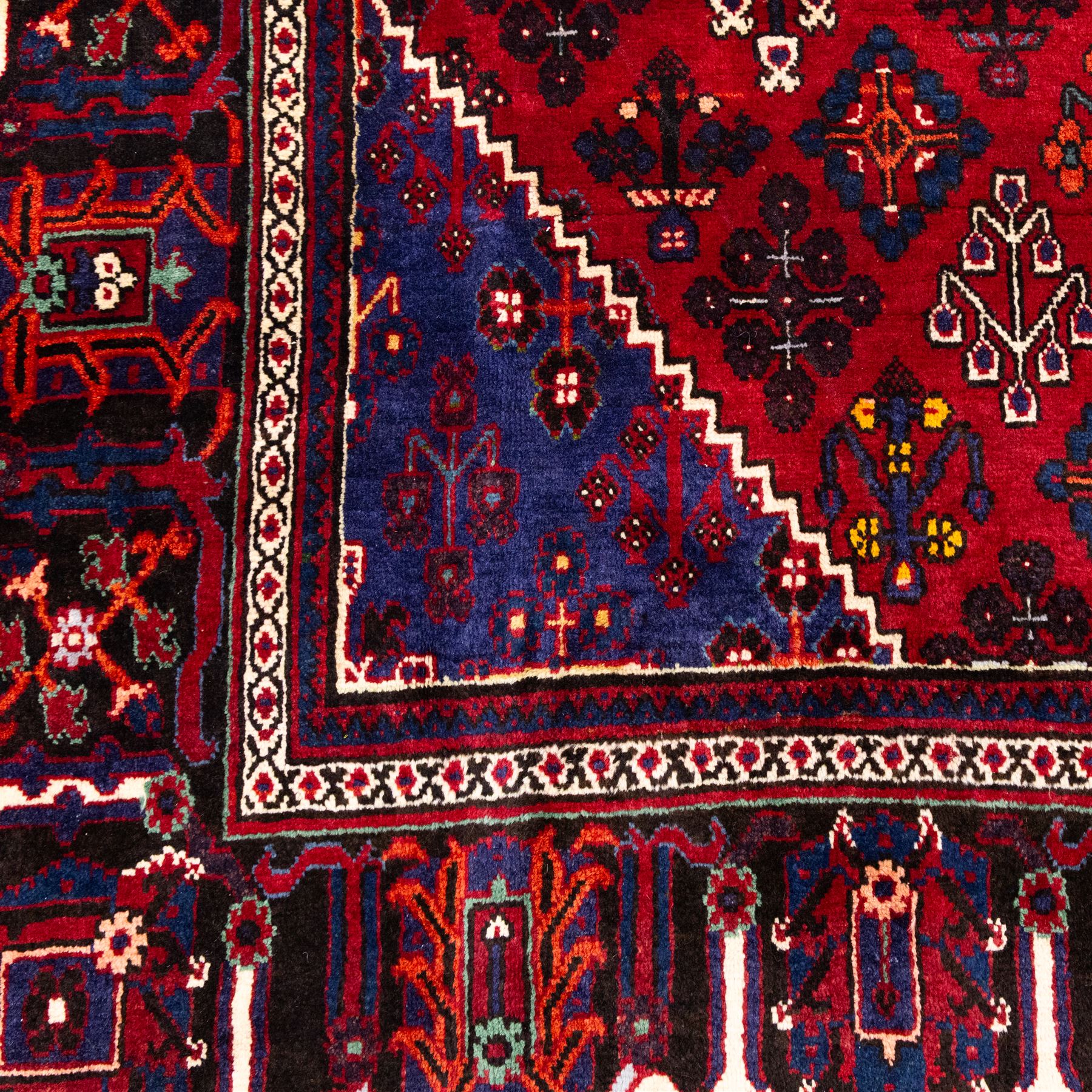Central Persian Joshagan hand-knotted rug, madder-red field with central stepped lozenge medallion enclosed by angular spandrels, field decorated with repeating stylized geometric floral motifs and small diamond devices enclosed by a dark border of geometric ornament between multiple guard stripes, with cotton fringe ends  