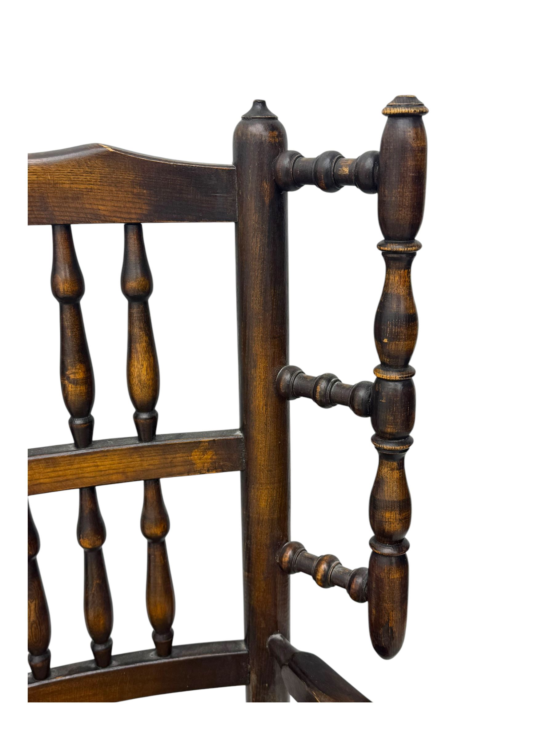 Early 19th century ash armchair, the back with winged spindles extending from a shaped top rail, above a splat of two rows of vertical spindles, with curved arms and a rush seat, raised on turned supports united by double stretchers terminating in castors
