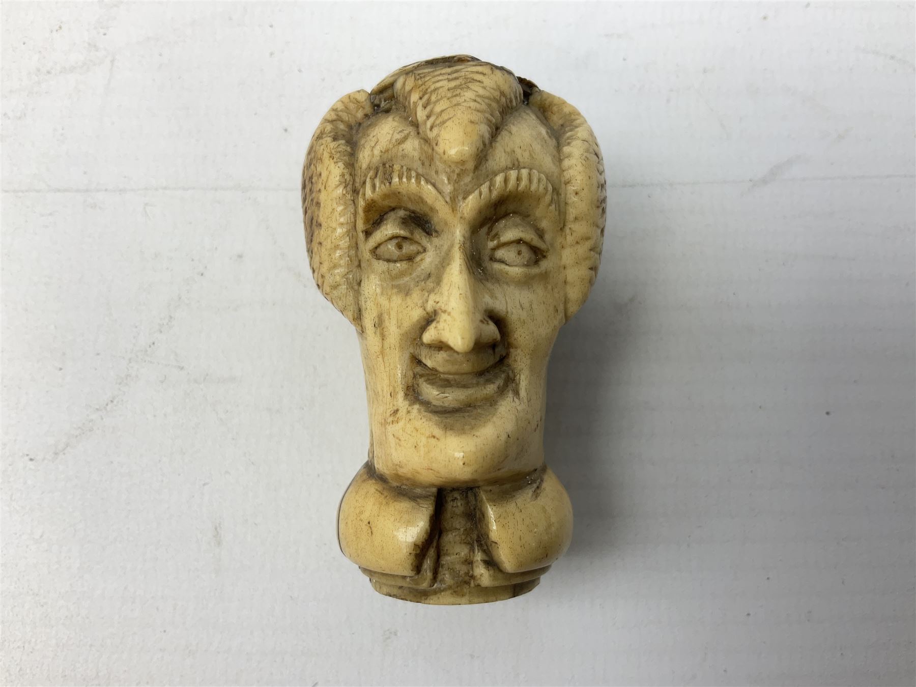 19th century carved ivory walking cane handle, modelled as the head of a greyhound with inset glass eyes, together with a further 19th century ivory example, modelled as a caricature of a gentleman's head, (2)
