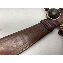 Mandingo sword with 63cm plain curving steel blade and leather covered grip with white metal ribbed spherical pommel; in decorative leather leaf scabbard with plaited tassels and shoulder strap L78cm overall