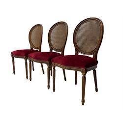 Set six French style walnut finish dining chairs, oval cane bergere backs over serpentine seats upholstered in red, flower head carved fluted supports