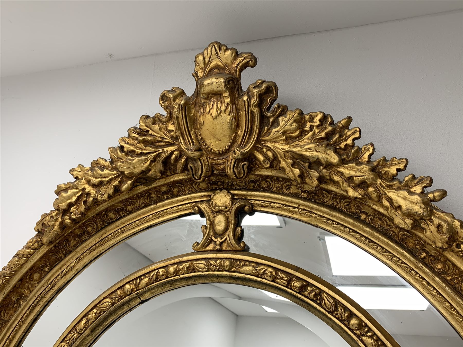 Gilt Rococo style mirror, arched top with central cartouche and oak leaf moulded pediment, floral and fruit moulded surround with segmented glass panels, bevelled central pane, c-scroll shell and acanthus leaf brackets