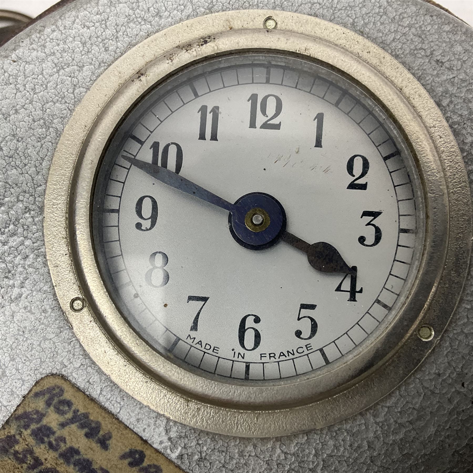 Metal cased drum shaped travelling clock with grey hammered finish, French clockwork movement and stitched leather outer case with shoulder strap; bears manuscript label 'Royal Armament Research and Development Establishment - serial no.09433' D13cm overall