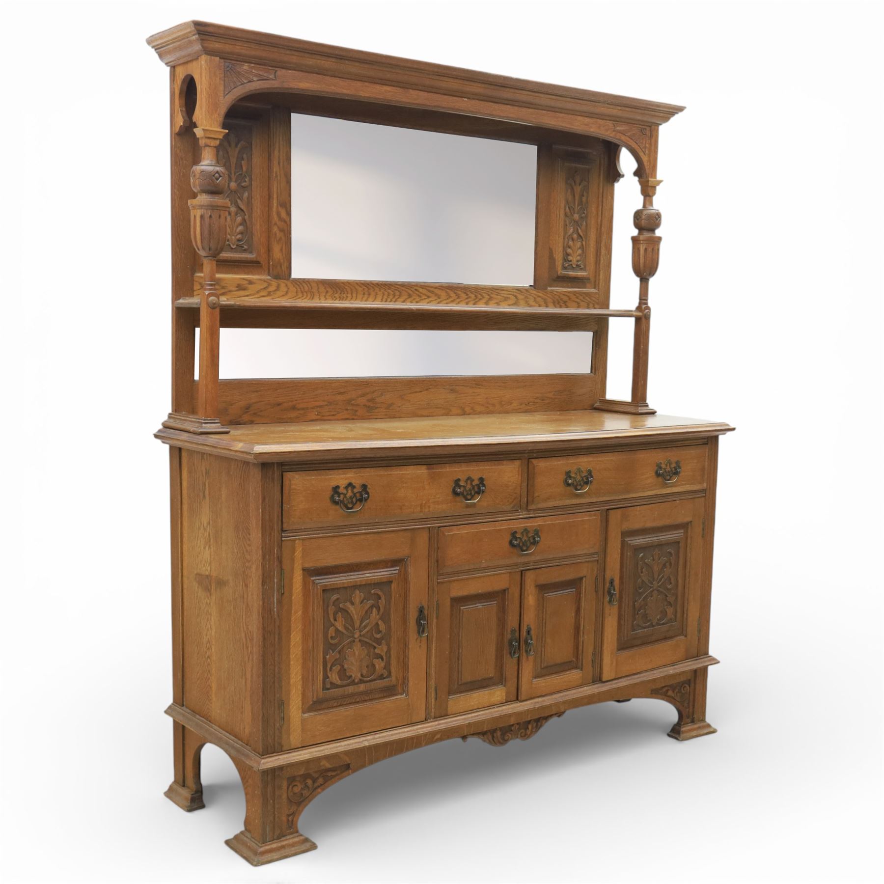 Arts and Crafts oak mirror back sideboard, the bevelled rectangular mirror set within a back with foliate carved panels, with turned baluster and knopped supports, upon a base with moulded top above three drawers  and three cupboard doors, two with carved foliate detail, upon four shaped bracket feet