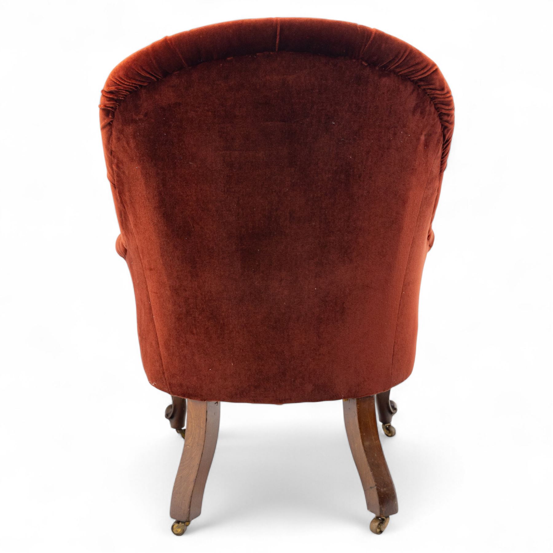 Victorian mahogany framed crimson velvet upholstered tub armchair, with buttoned back and scroll carved arms above a serpentine fronted seat rail, raised upon scroll carved cabriole front legs and plain curved back legs with brass castors 