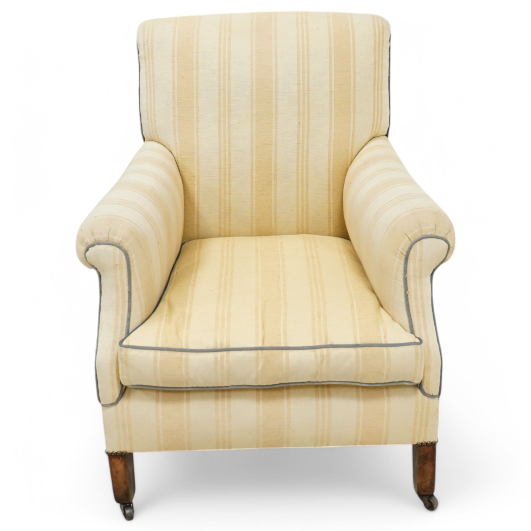 Early 20th century scroll arm armchair, upholstered in ivory striped cotton fabric with piped seams, sprung seat, on turned tapering front legs with brass caps and castors