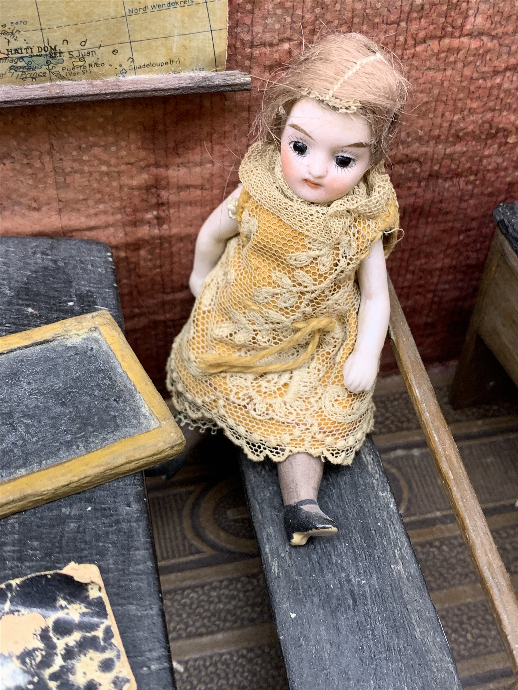 Late Victorian wooden school room setting with bisque head teacher and six German all bisque pupils each seated at a combined desk and chair with slate board, in a classroom furnished with chest of drawers, fire-surround, lectern, wall map, pictures, miniature books, school bell, chalk board on easel, wall clock etc, L70cm H28cm D28cm
