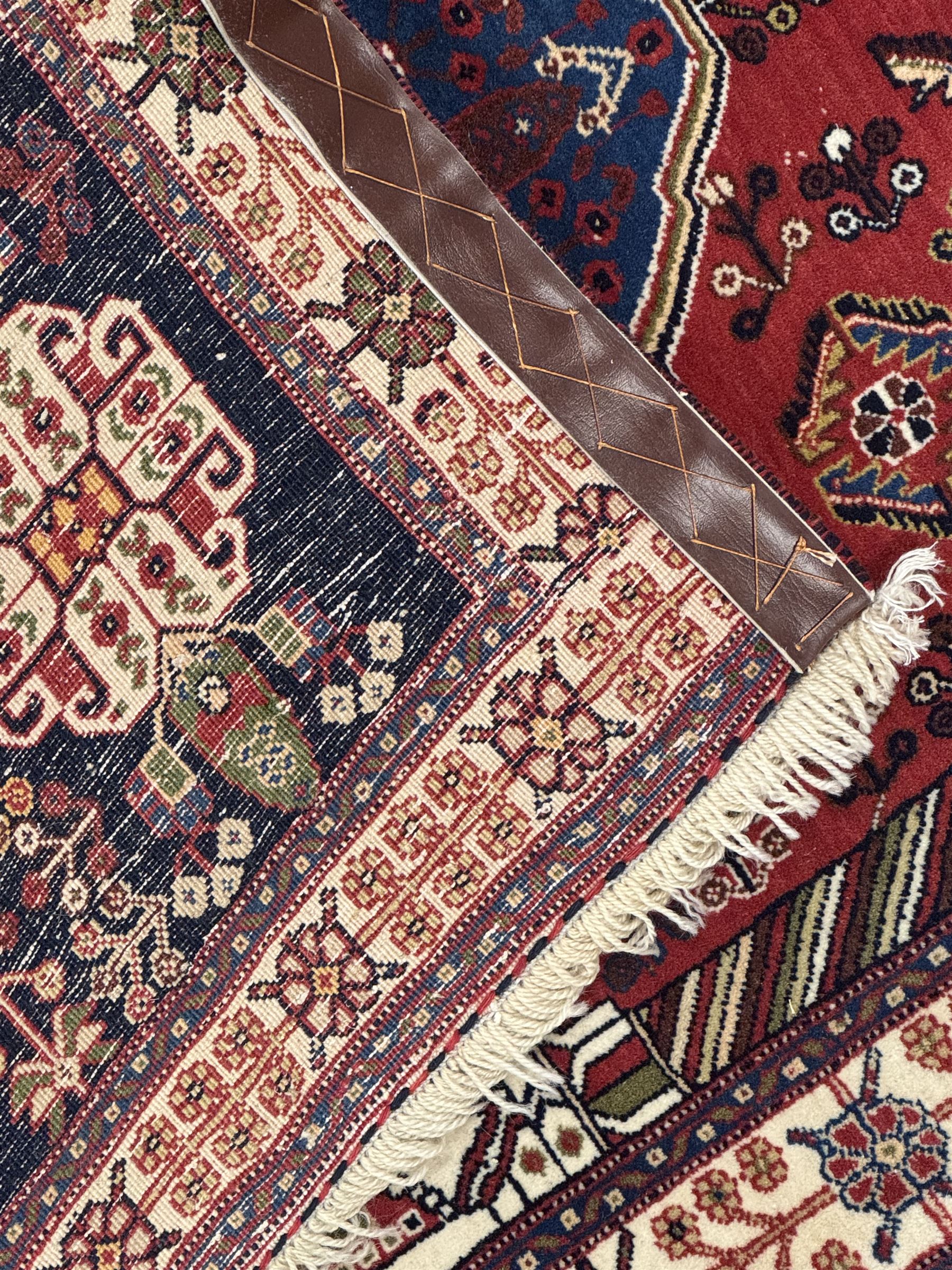 Fine Persian Qashqai crimson and navy ground runner, three large medallions filled with geometric and floral designs, the field with angular vines and stylised floral decoration, wide ivory border decorated with repeating floral and angular motifs