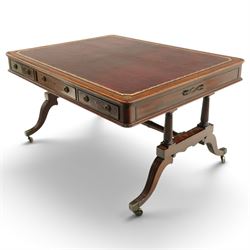 Regency inlaid mahogany and brass mounted library table, the rectangular top inset with gilt tooled burgundy leather writing surface, enclosed by  crossbanding and boxwood stringing with roundel corner motifs, above three cock-beaded frieze drawers to either side fitted with brass ring handles and brass escutcheons, the end friezes centred by applied brass foliate mounts, raised on twin reeded column supports over rectangular platform ends, united by a ring-turned stretcher, the reeded sabre legs terminating in brass caps and castors, one drawer bearing ivorine label 'Spillman & Co., St Martins Lane, London'