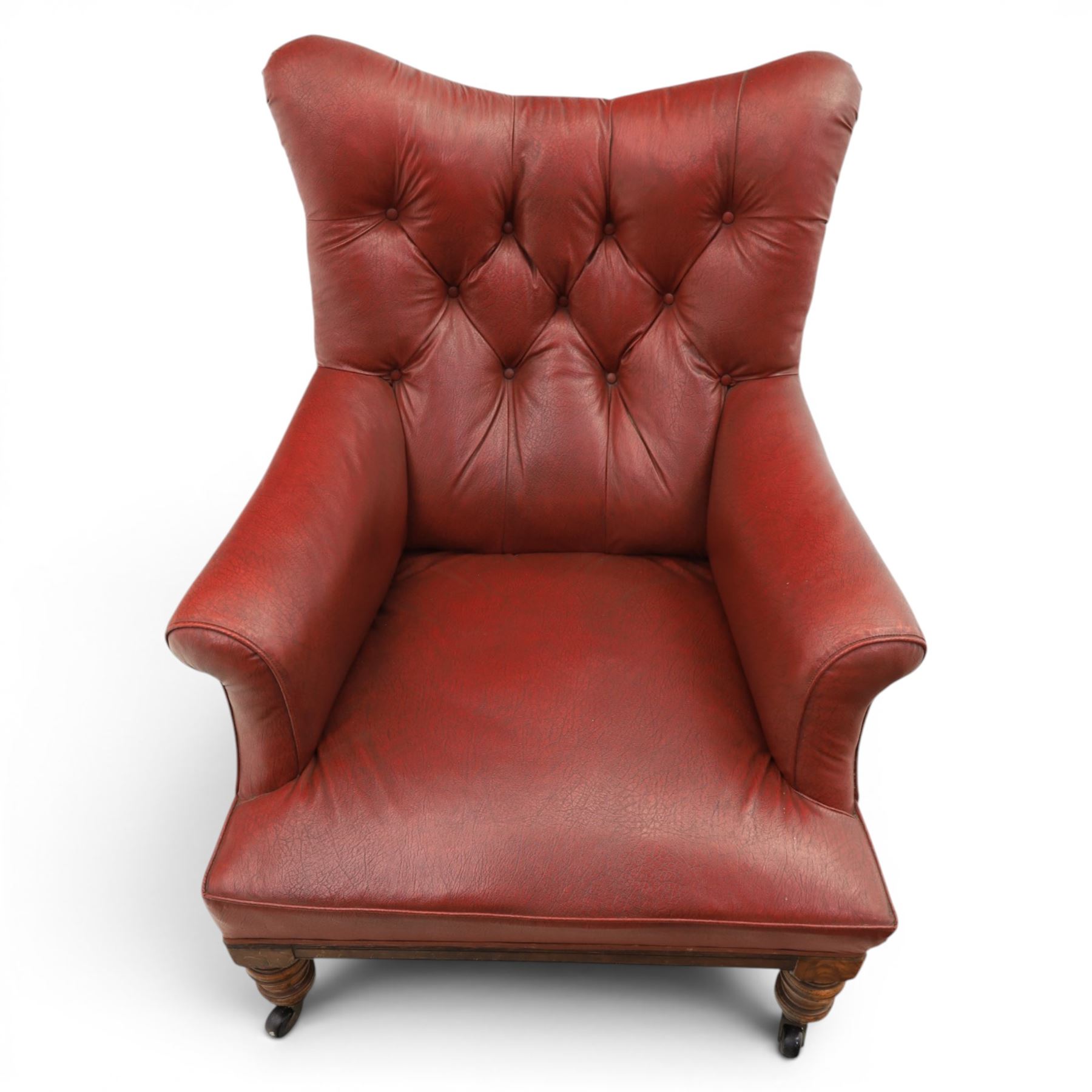 Early 20th century style oxblood red leather Chesterfield armchair, deep buttoned shaped back over padded scroll arms and loose seat cushion, raised on turned mahogany front supports with brass caps and castors