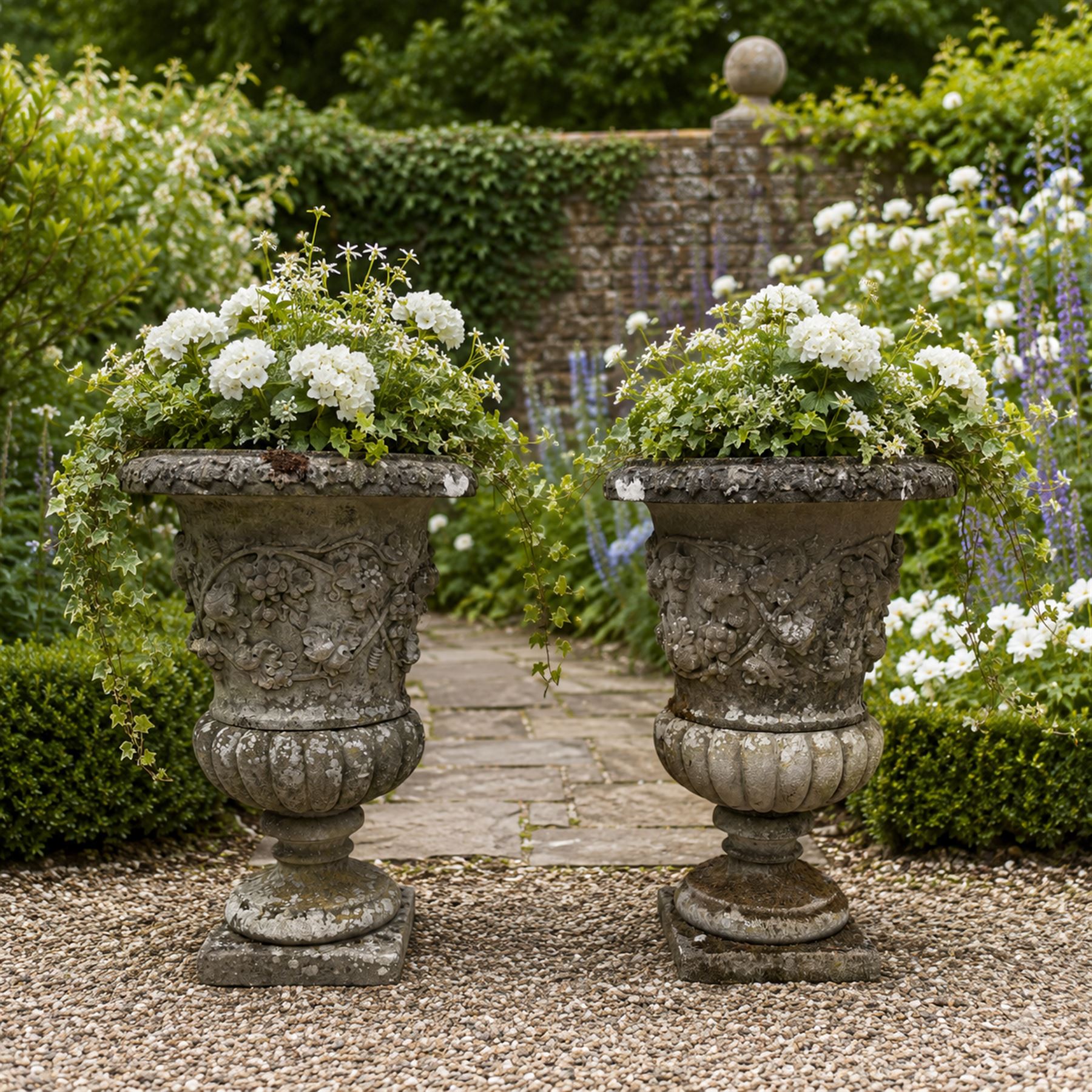 Pair of quality antique weathered three-piece composite stone garden urns, the flared rim moulded with repeating acanthus leaves, over a deep-relief campana body decorated with fruiting grapevines and ivy leaves, the gadrooned underbelly over a turned socle and square base