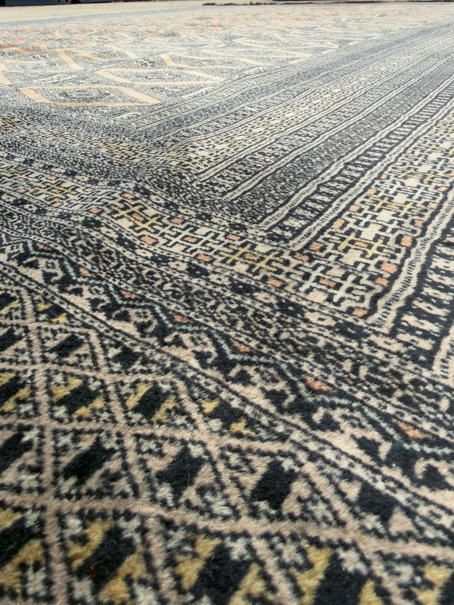Large Persian Bokhara wool rug, the field decorated with repeating gul motifs in lozenge medallions across a dark ground, enclosed by multiple geometric borders in indigo, ivory and terracotta, from the region of Baluchistan