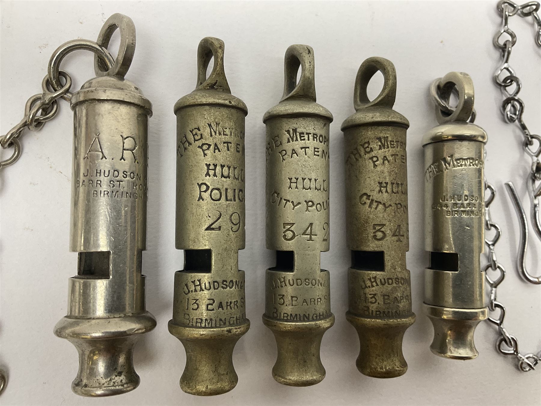 Three Hull City Police 'Metropolitan' whistles by J. Hudson 13 Barr Street Birminham, each with impressed collar number; another 'Metropolitan' police whistle with chain; and an ARP whistle by Hudson & Co with chain (5)