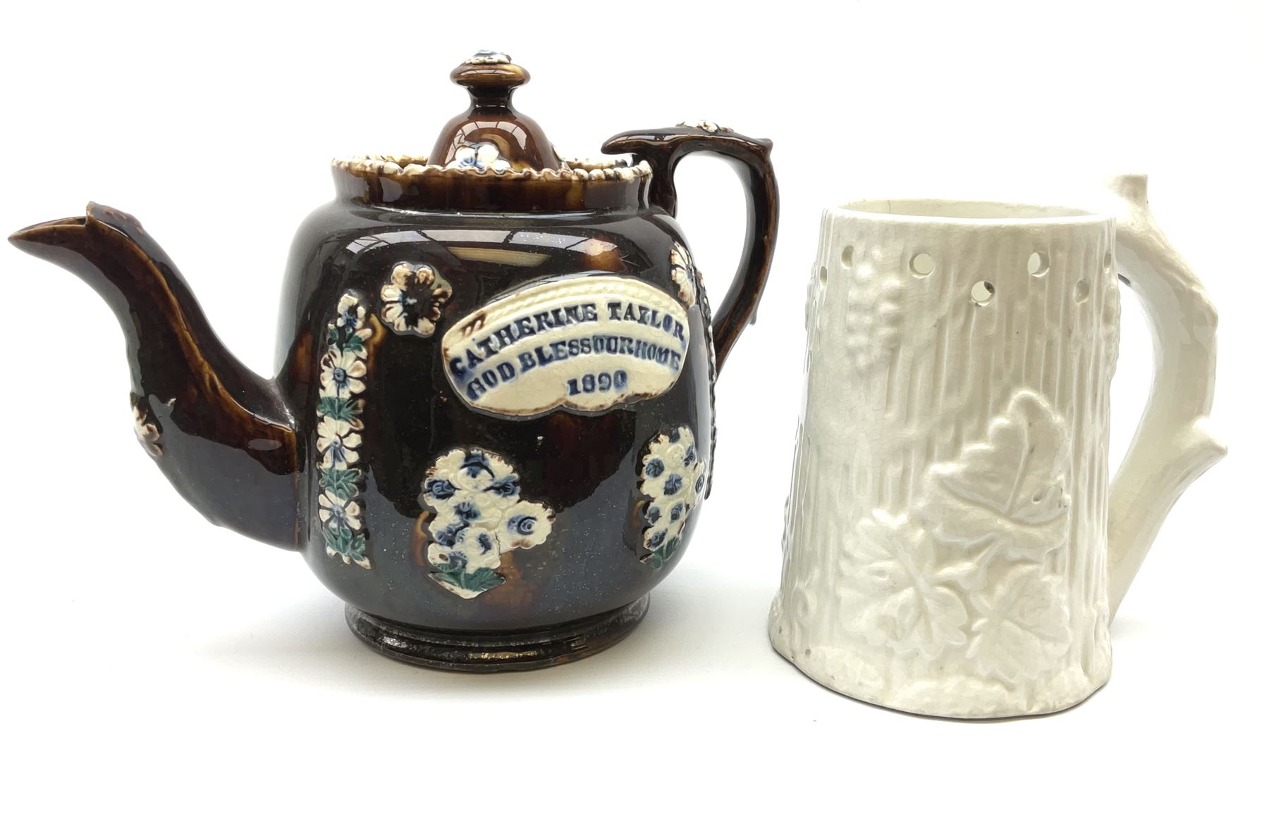 A 19th century Barge Ware teapot, decorated with applied floral sprays and thistles against a mottled brown ground, and plaque detailed Catherine Taylor God Bless Our Home 1890, H18cm, together with a white glazed puzzle mug, H15cm. 
